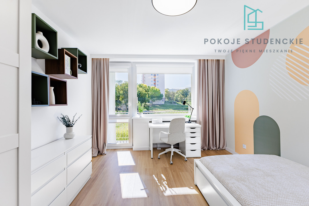 Bright student bedroom with white furniture, pastel wall arches, and a desk by a large window overlooking greenery.