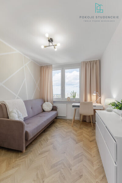 Cozy student living room with lavender sofa, geometric wall pattern, and a white desk by the window.
