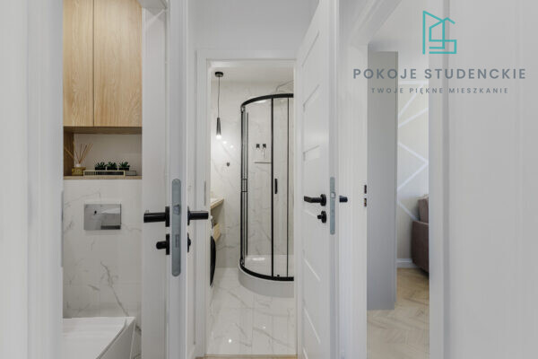 Open doors reveal a modern hallway leading into a marble bathroom with a curved glass shower enclosure.