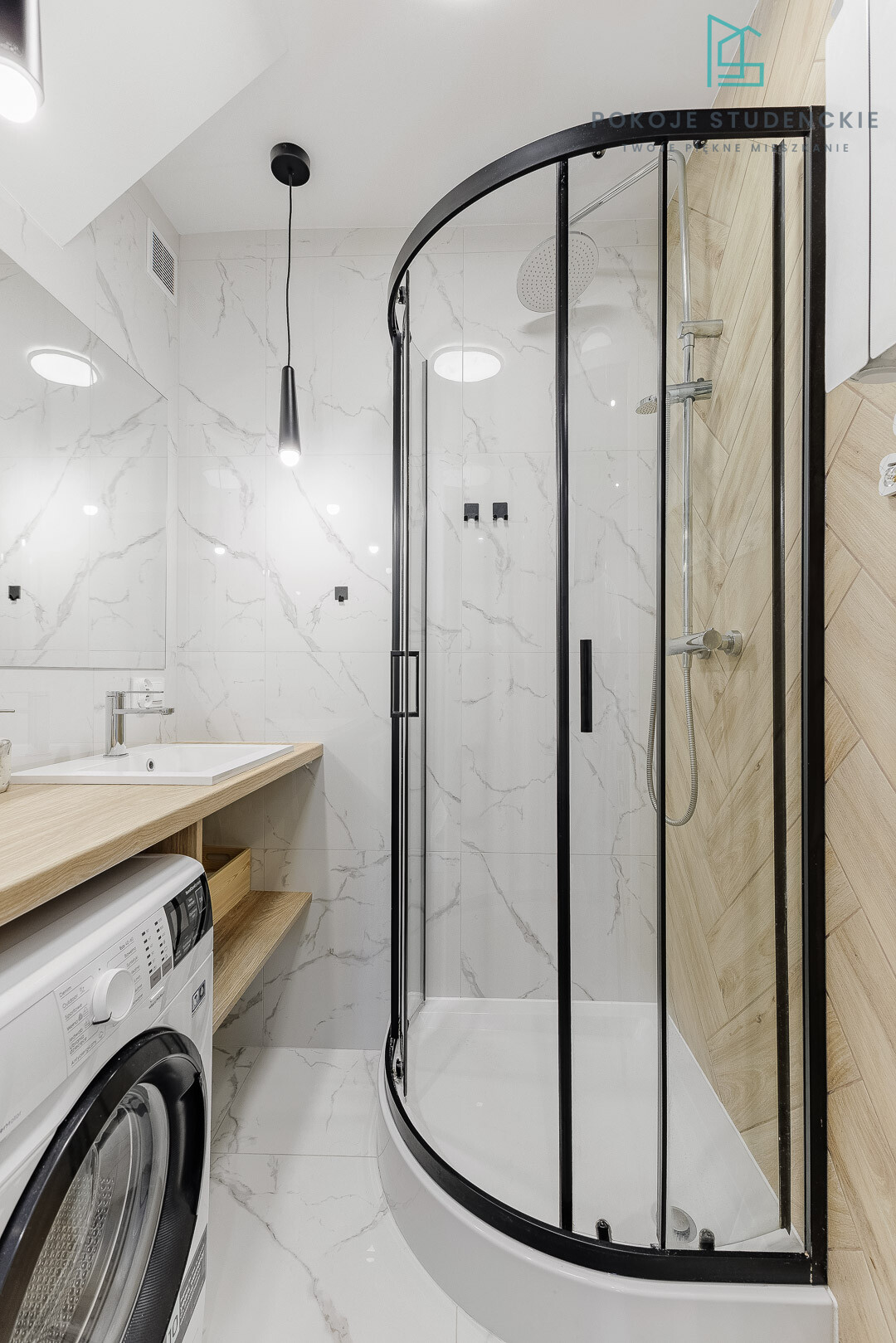 Modern bathroom featuring a curved glass shower enclosure, black framed doors, white marble walls, and a wooden vanity with a front-loading washing machine beneath.