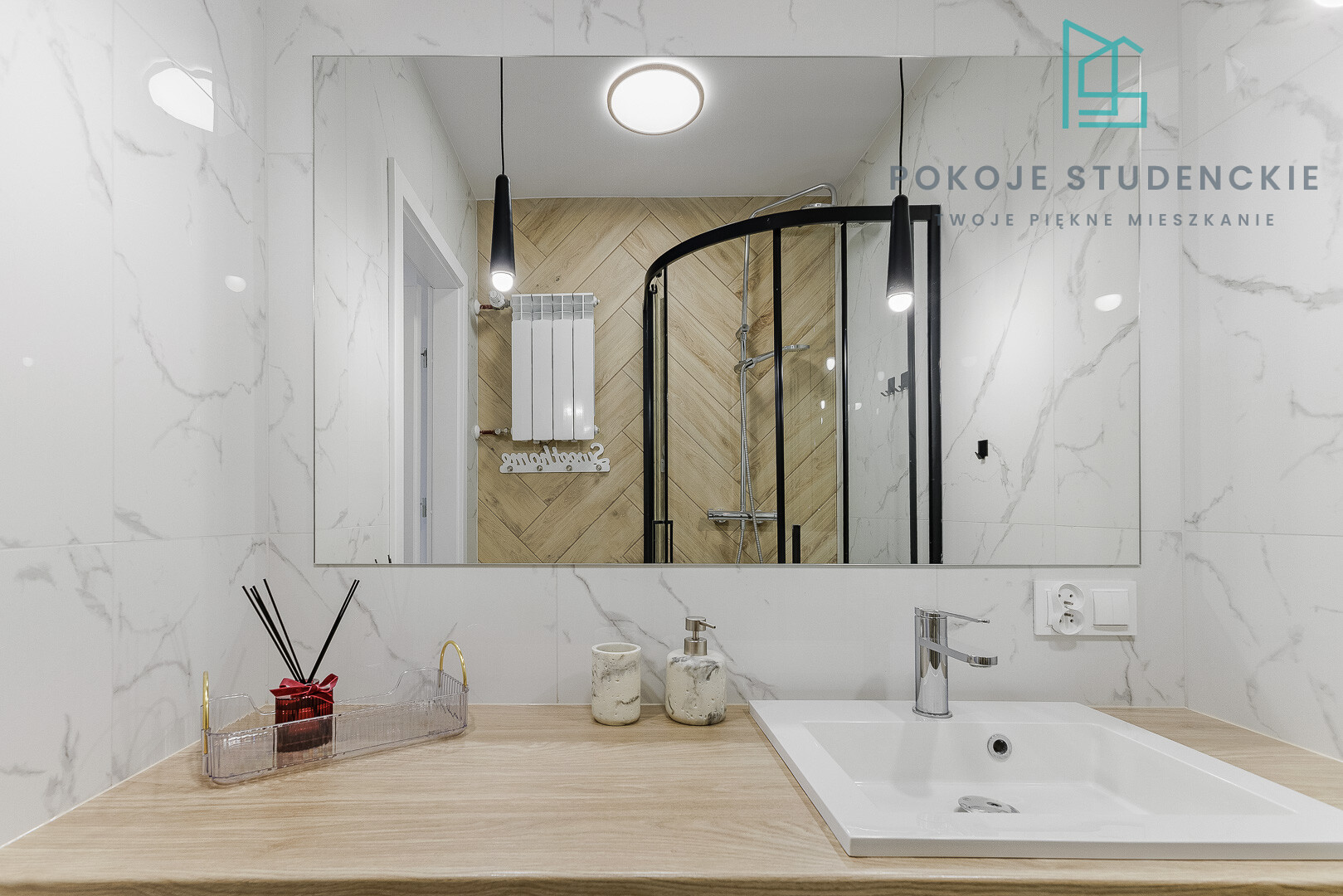 Modern bathroom vanity with a light wood countertop, white sink, and chrome faucet, marble walls, and a large mirror reflecting a glass shower enclosure with a wooden-tile accent wall; logo text appears in the upper right corner.