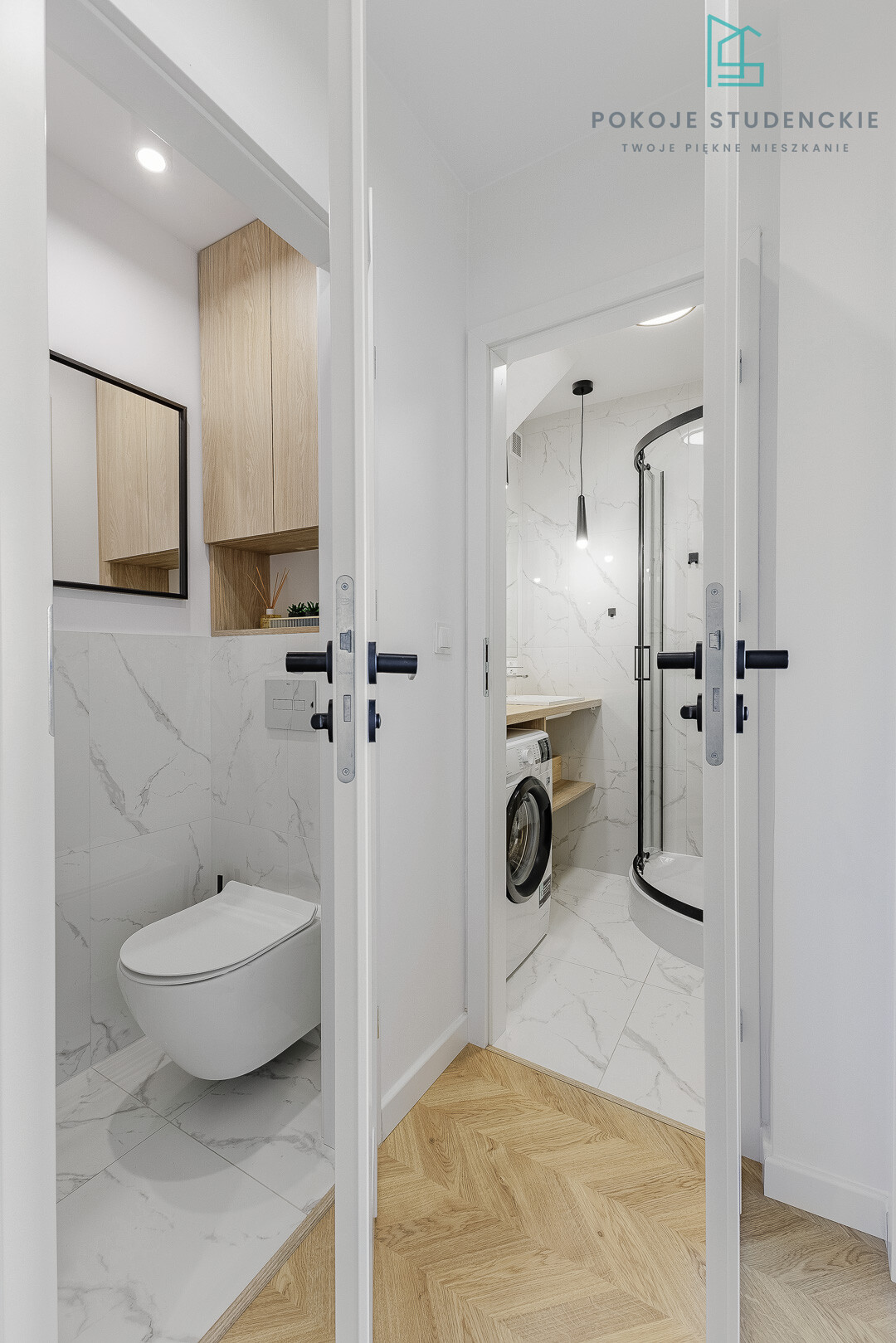 Open double doors reveal a compact modern bathroom: marble-tiled walls, wall-hung toilet, wooden cabinets, and a laundry area with a curved shower enclosure visible beyond.