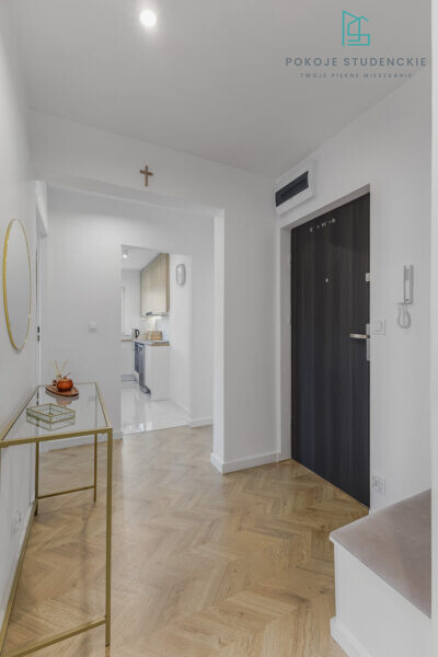 Bright modern hallway with herringbone wood floor, a small crucifix on the wall, and a view into the adjacent kitchen.