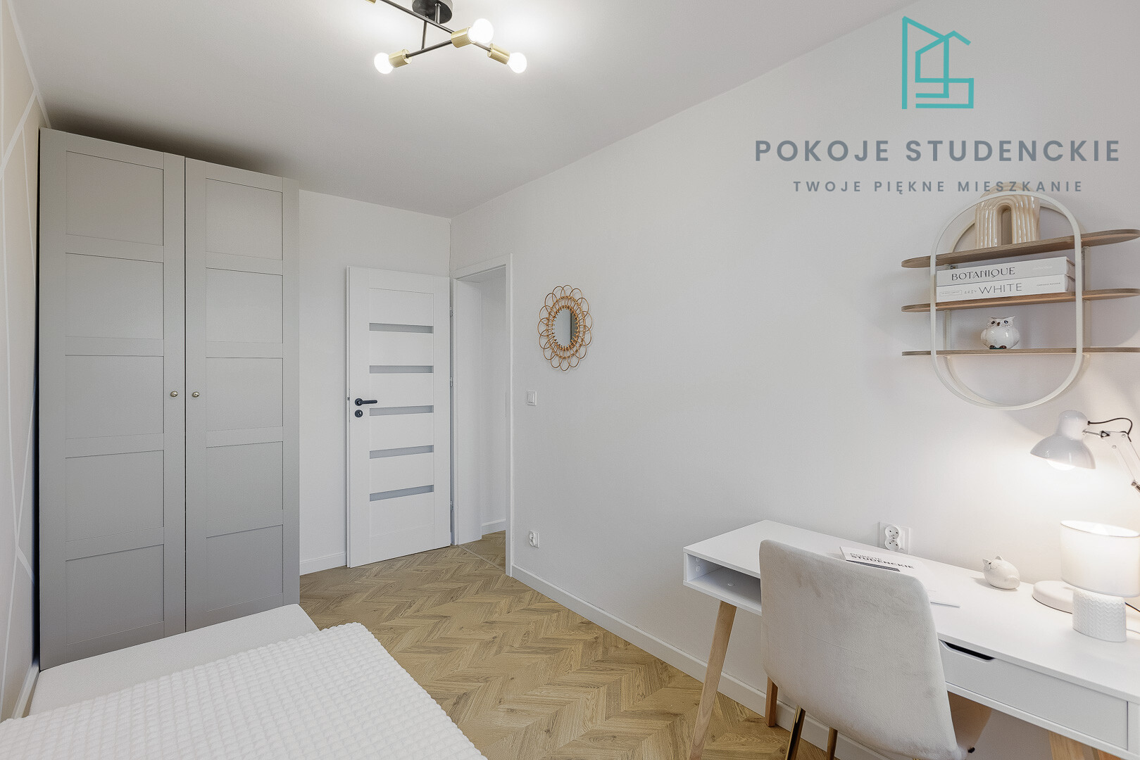 Minimalist student room with white walls, tall gray wardrobe, white door, and a white desk with a lamp on herringbone wood floor.