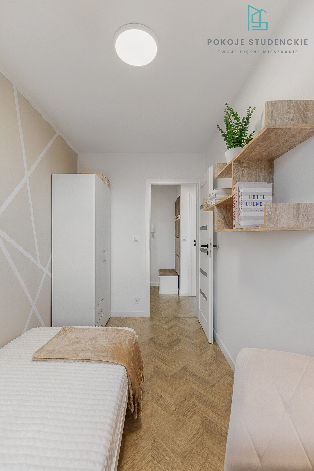Bright student room with a single bed, white wardrobe, wooden wall shelves, and a potted plant; logo in the top-right corner.