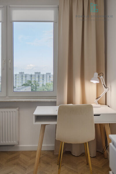 Bright home office corner with a white desk, beige chair, and adjustable white desk lamp by a large window.