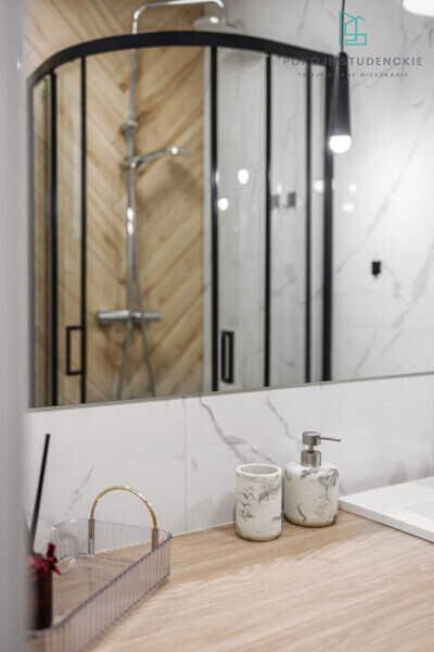 Modern bathroom vanity with marble countertop, soap dispenser, and toothbrush cup; curved glass shower enclosure in background