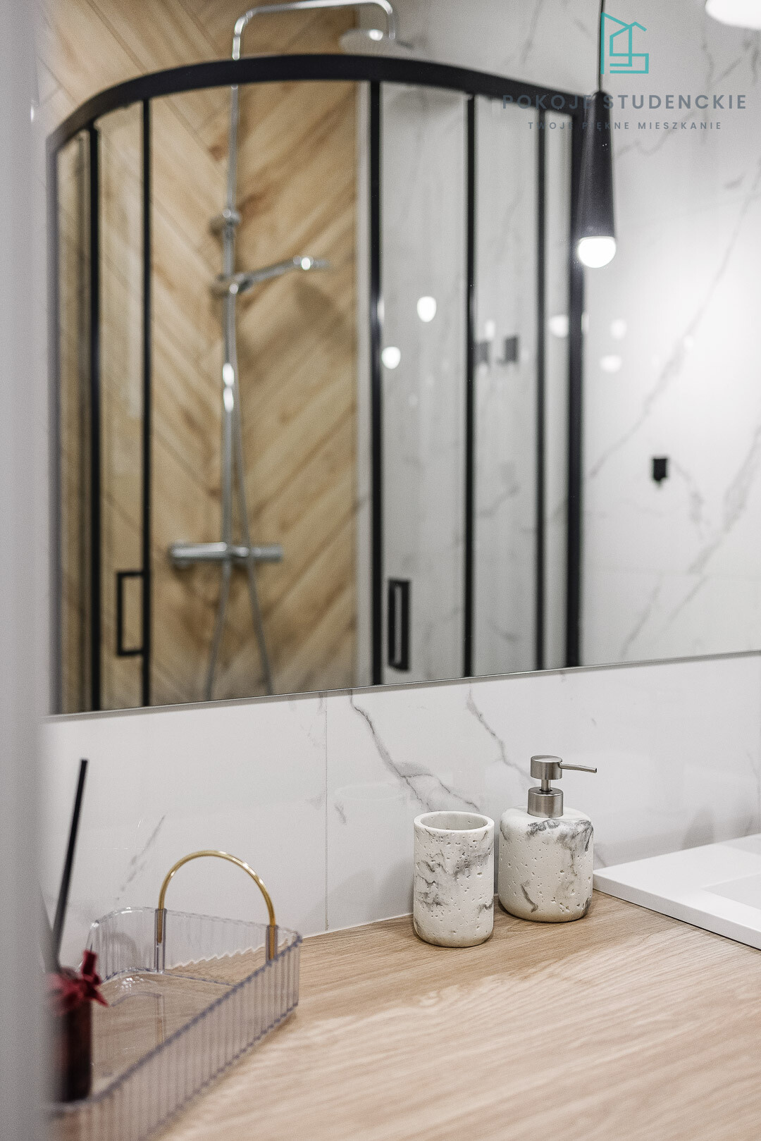 Modern bathroom vanity with marble countertop, soap dispenser, and toothbrush cup; curved glass shower enclosure in background