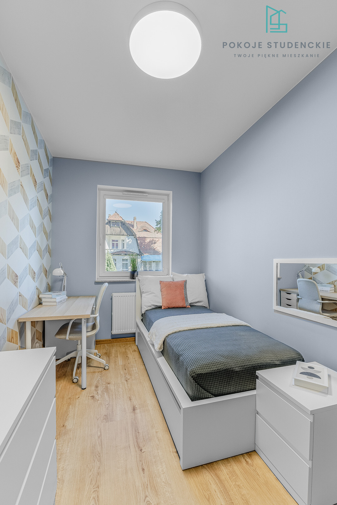 Single bed against blue wall with a desk and chair by a window, geometric wallpaper on the left and a light wood floor.