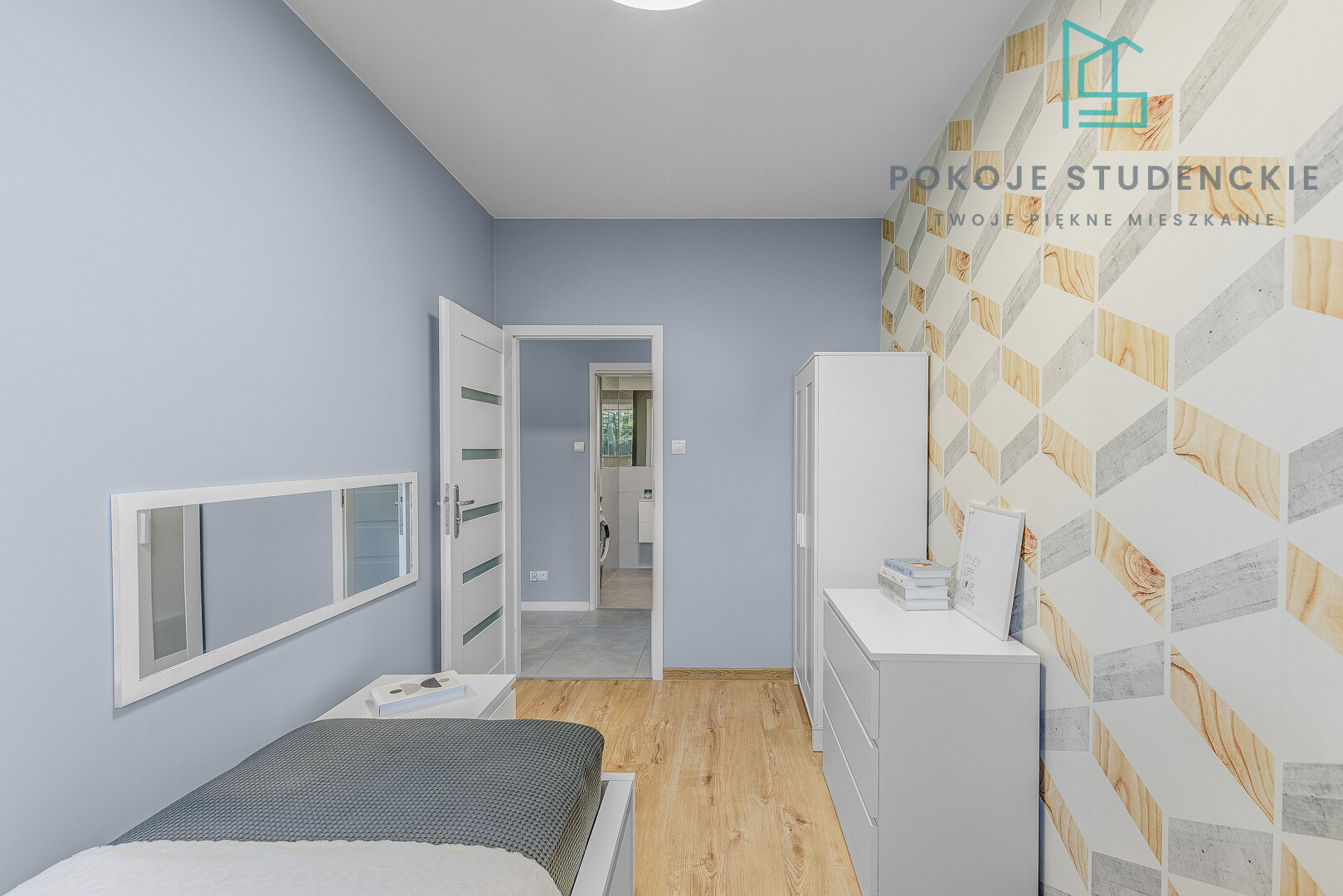 Modern student bedroom with blue walls, white furniture, and a geometric wood-pattern wallpaper on the right; logo in the top-right corner.