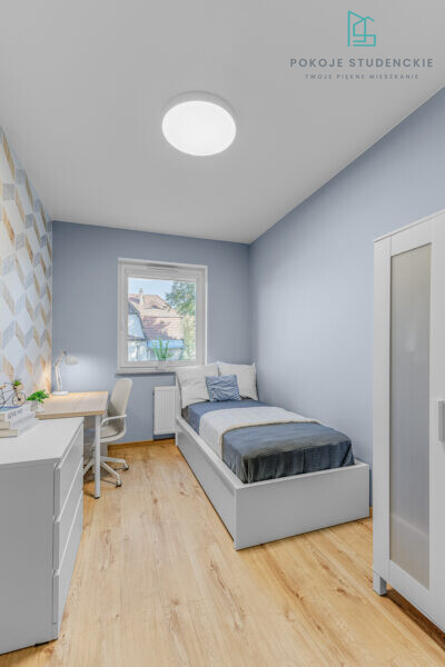 Cozy blue-toned bedroom with a single bed, desk and chair, window view of houses outside.
